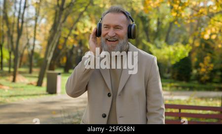 Glücklicher sorgloser, fröhlicher alter Mann kaukasischer männlicher Senior mittleren Alters reifer pensionierter Geschäftsmann hören Musik in kabellosen Kopfhörern Ohrhörern in der Stadt genießen Stockfoto