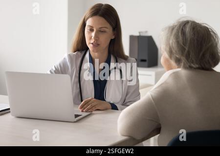 Die Ärztin benutzt einen Laptop, wenn sie sich mit einer alten Patientin trifft Stockfoto