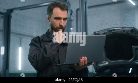 Ernsthaft fokussierter Kaukasier Guy Techniker Automechaniker Ingenieur prüfen Reparatur Autoproblem Computerdiagnose Elektromotor mit Stockfoto