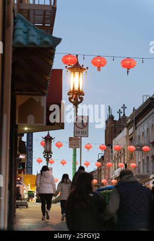 Fußgänger laufen eine Straße in Chinatown, San Francisco, CA, entlang, gesäumt von traditionellen roten Laternen und einem chinesischen Leuchtenpfosten. Stockfoto