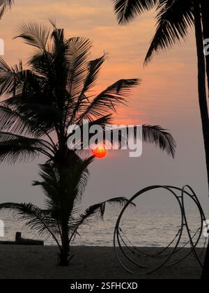 Sonnenuntergang über dem Arabischen Meer durch Palmen an einem wunderschönen einsamen Strand in NIleshwar im Bundesstaat Kerala - Indien Stockfoto