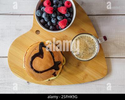 Valentinstag-Frühstück. Herzförmiges Tablett, Espresso und Pfannkuchen mit einem gezogenen Schokoladenherz. Stockfoto