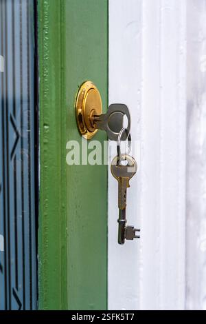 Nahaufnahme von Schlüsseln in der grün bemalten Holztür eines Hauses, andere hängen am Schlüsselring. Stockfoto