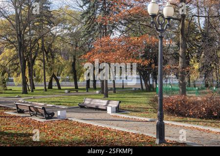 Minsk, parken Sie am Fluss Svisloch. Laterne im Vordergrund, Fußgängerwege und Bänke. Spätherbst. Stockfoto