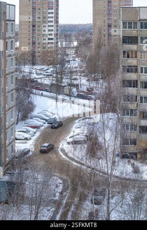 Blick von oben auf den Innenhof eines Wohngebäudes, einen Parkplatz mit schneebedeckten Autos und eine Straße in einem Wohngebiet von ​​Minsk. Der Ring r Stockfoto