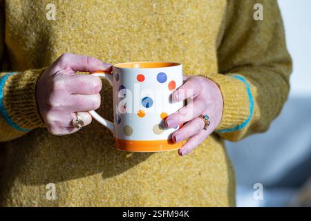 Bristol, Großbritannien. Eine Frau, die eine große Tasse Tee oder Kaffee hält. Der schwere heiße Becher wird von beiden Händen gestützt Stockfoto