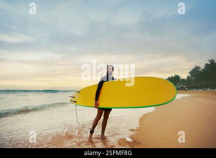 Junger bärtiger Mann mit Surfbrett, der in der Nähe eines Strandes steht. Mann mit Surfbrett im Freien an einem Sommertag. Stockfoto