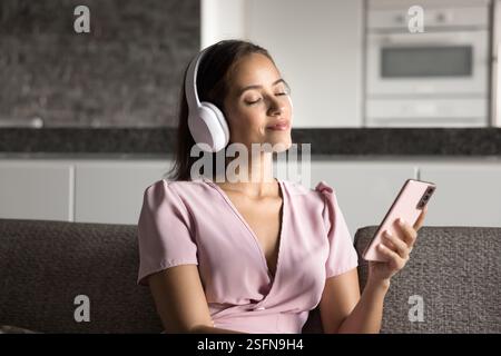 Frau sitzt auf dem Sofa und genießt Musik mit ruhigem Ausdruck Stockfoto