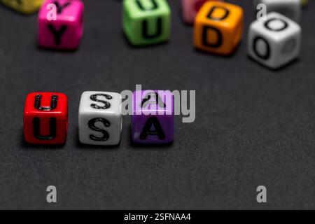 Kleine farbige Würfel mit Buchstaben bilden im Vordergrund das Wort „USA“ (USA), schwarzer Hintergrund, Kopierraum. Stockfoto