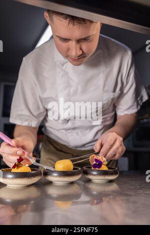 Professioneller Koch garniert kleine Gerichte mit essbaren Blumen und Schinken in einer Restaurantküche Stockfoto