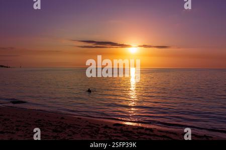 Sehr farbenfroher Sonnenuntergang über dem indischen Ozean Horizont, die Silhouette eines jungen Menschen schwimmt im Wasser in der Ferne, Mauritius Island Stockfoto
