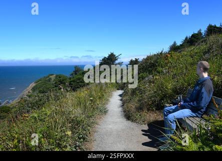 Junger Mann ruht und genießt die Aussicht vom Port Orford Heads Trail an der Küste von Oregon. Der Weg kann in die Distanz fortgesetzt werden. Er hat auf blauem J Stockfoto