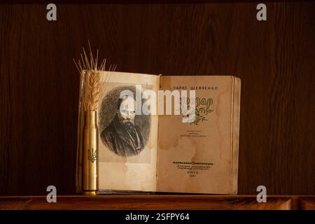 Ukraine Dnepr 9. Februar 2025 - Buch Kobzar Taras Schewtschenko und ein Kartuschenetui mit dem Wappen der Ukraine und einem Weizenohr auf einem Regal Stockfoto