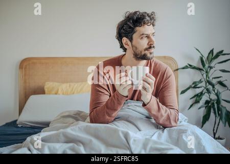 Entspannter junger gutaussehender Mann aus dem Nahen Osten, der morgens Kaffee im Bett genießt. Stockfoto