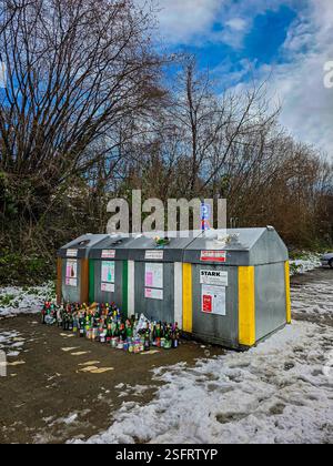 Viele leere Flaschen und Gläser neben den überfüllten Behältern für die getrennte Sammlung von Glas nach Feiertagen. Januar 2025. Uberlingen, Deutschland Stockfoto