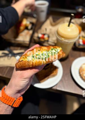 Croissant-Sandwich mit Eierhaltung in der Hand im Café-Shop-Restaurant, serviert auf Tablett. Stockfoto