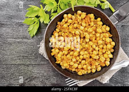 Kichererbsen, die mit Sellerie, Tomaten, Zwiebeln, Karotten und Knoblauch in einer Bratpfanne auf Sacktuch auf dunklem Holzbrett von oben geschmort werden Stockfoto