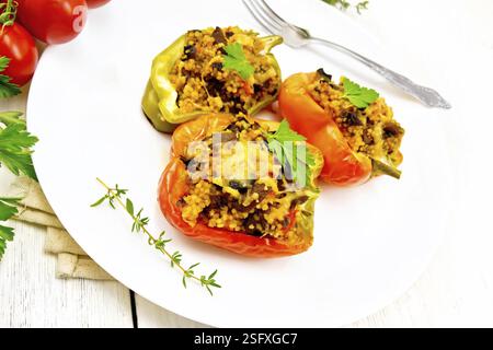 Paprika süss, gefüllt mit Pilzen, Tomaten, Couscous und Käse in einer weißen Platte auf Küchenpapier, Gabel, Petersilie vor dem Hintergrund des Lichts w Stockfoto