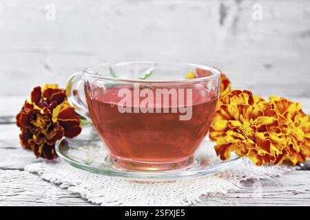Ringelblume Kräutertee in einer Glasschale und Untertasse auf einer Serviette aus Sacktuch, frische Blumen auf Holzbrett Hintergrund Stockfoto