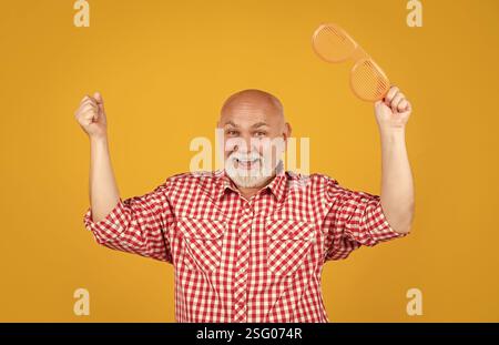 Froher älterer Mann mit Partybrille auf gelbem Hintergrund Stockfoto