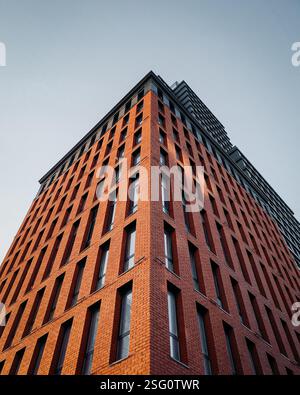 Blick auf die Fassade eines modernen Gebäudes mit Ziegelfassade. Ecke eines stilvollen Wohngebäudes bei Sonnenuntergang vor klarem blauem Himmel. Stockfoto