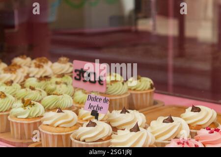 Bunte Cupcakes in einem Bäckereifenster. Die Cupcakes werden mit Zuckerguss belegt, mit Aromen wie Dulce de Leche und Pistazien. A Stockfoto