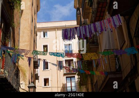 Eine enge Straße in einer Stadt mit farbenfrohen Papel-Picado-Dekorationen, die zwischen Gebäuden hängen. Der Himmel ist oben sichtbar, und die Architektur ist mit Ba ausgestattet Stockfoto