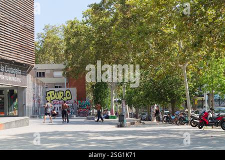 Eine lebhafte urbane Szene, in der Menschen in einem parkähnlichen Bereich mit Bäumen, Graffiti an Wänden und einer Mischung aus Fahrrädern und Motorrädern in der Nähe spazieren gehen. Stockfoto