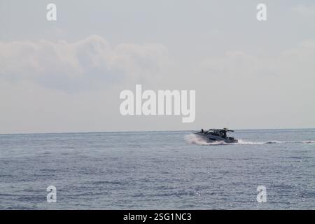 Ein kleines Boot, das auf ruhigen Gewässern unter einem bewölkten Himmel fährt. Das Boot hinterlässt eine Spur aus weißem Schaum, während es sich schnell über die Oberfläche bewegt. Stockfoto