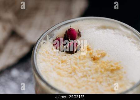 Cremiger Latte mit Kokosflocken und getrockneter Rosengarnitur, serviert in einem Glas mit samtiger Schaumplatte Stockfoto