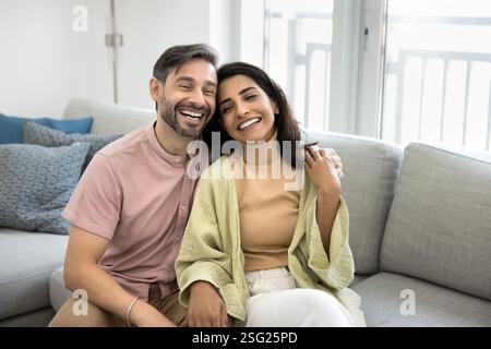 Das junge Paar sitzt auf dem Sofa, lacht und genießt die Gesellschaft Stockfoto