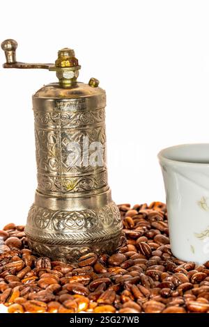 Vintage-Handkaffeemühle mit kunstvollem Metalldesign und weißer Porzellanschale auf gerösteten Kaffeebohnen Stockfoto