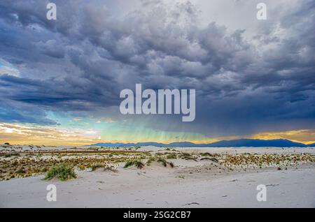 Dramatische Sturmwolken über dem White Sands National Park, New Mexico, mit Regen in der Ferne und goldenem Licht, das die Dünen erleuchtet. Stockfoto