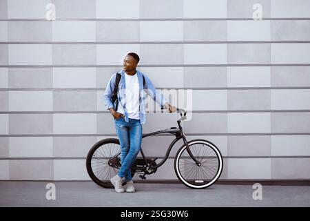Attraktiver afroamerikanischer Kerl mit Fahrrad, das in der Nähe der Ziegelmauer auf der Stadtstraße steht, leerer Raum Stockfoto