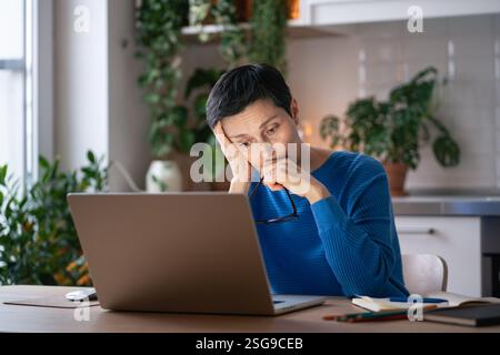 Verbrannte traurige Frau zu Hause, leidet unter Kopfschmerzen durch übermäßige Bildschirmzeit und Arbeitsstress am Laptop Stockfoto
