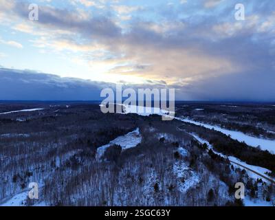 Eine riesige, schneebedeckte Waldlandschaft mit einer Straße, die durch das Zentrum führt, ist von oben unter den tiefblauen und rosa Wolken der Dämmerung zu sehen Stockfoto