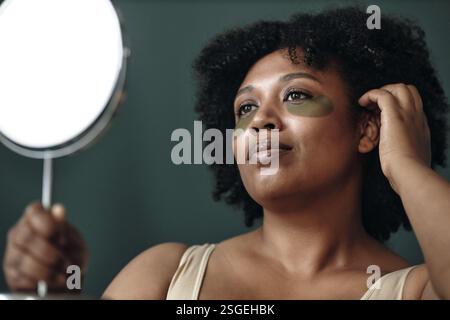 Porträt einer Frau, die Gesichtsmaske Creme mit Spiegel aufträgt Stockfoto