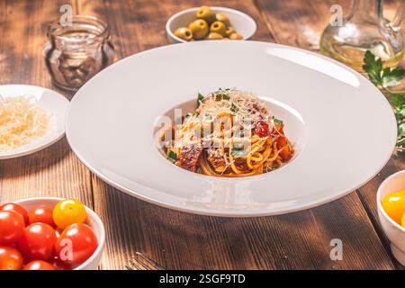Spaghetti Puttanesca nach einem traditionellen italienischen Rezept mit Sardellen, Oliven, Kapern auf einer weißen Platte auf einem hölzernen Hintergrund mit Zutaten Stockfoto