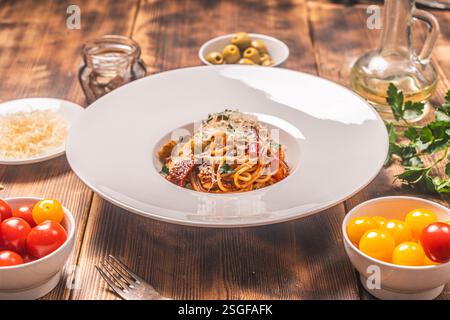 Spaghetti Puttanesca nach einem traditionellen italienischen Rezept mit Sardellen, Oliven, Kapern auf einer weißen Platte auf einem hölzernen Hintergrund mit Zutaten Stockfoto