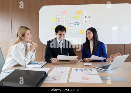 Verschiedene Geschäftsteams arbeiten an einem Schreibtisch zusammen, analysieren Berichte und diskutieren Strategien in einer modernen Büroumgebung. Stockfoto