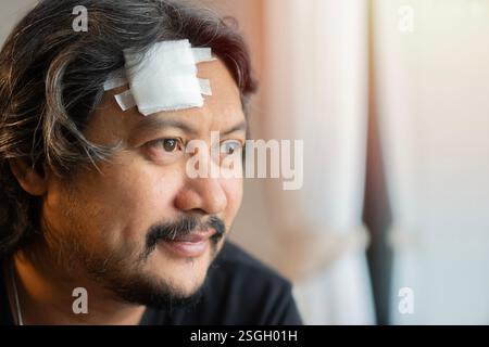 Seitenansicht Porträt eines glücklichen Erwachsenen asiatischen Mannes mit Bandage auf der Stirn, schauen Sie nach vorne und fühlen Sie sich besser. Kopierbereich. Stockfoto