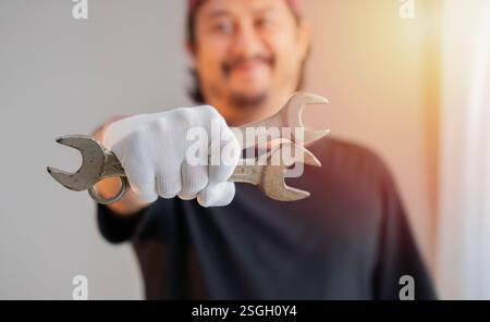Die Hand des Mannes trägt weiße Stoffhandschuhe und hält einen Schraubenschlüssel auf dem Hintergrund des Sonnenlichts. Nahaufnahme. Stockfoto