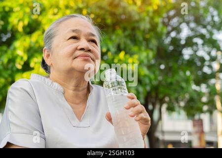 Die alte Asiatin trinkt Wasser nach dem Spaziergang im Park. Das Konzept eines gesunden Lebensstils. Kopierbereich Stockfoto