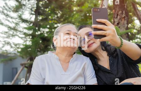 Fröhliche Erwachsene Tochter und Mutter sitzen auf der Bank und machen Selfie im Park. Selektiver Fokus, Kopierraum. Stockfoto