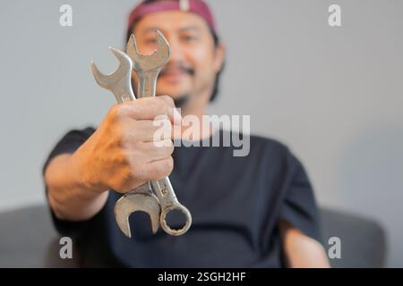 Lächelnder asiatischer Erwachsener mit Schraubenschlüsseln an den Händen, um sein Auto zu Hause zu reparieren. Selektiver Fokus. Stockfoto