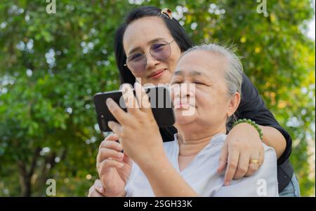 Fröhliche Großmutter und Enkelin haben Spaß mit sozialen Medien auf dem Handy im Park. Stockfoto