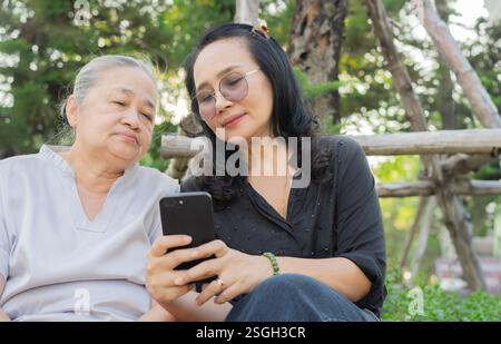 Glückliche ältere Frau und Tochter mit Handy, genießen Sie Outdoor-Freizeitaktivitäten im Naturpark. Stockfoto