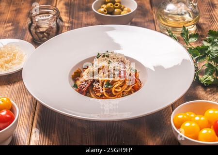 Spaghetti Puttanesca nach einem traditionellen italienischen Rezept mit Sardellen, Oliven, Kapern auf einer weißen Platte auf einem hölzernen Hintergrund mit Zutaten Stockfoto