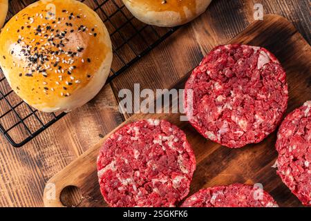 Ein amerikanischer Burger, gebackene Brötchen und rohes Rindfleisch-Burger-Patties auf hölzernem Hintergrund. Nahaufnahme. Blick von oben. Hochwertige Fotos Stockfoto