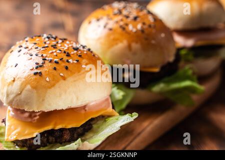 Drei Burger mit Patty, Käse und Salat auf Holzbrett und Hintergrund. Nahaufnahme. Leerzeichen für Text. Hochwertige Fotos Stockfoto